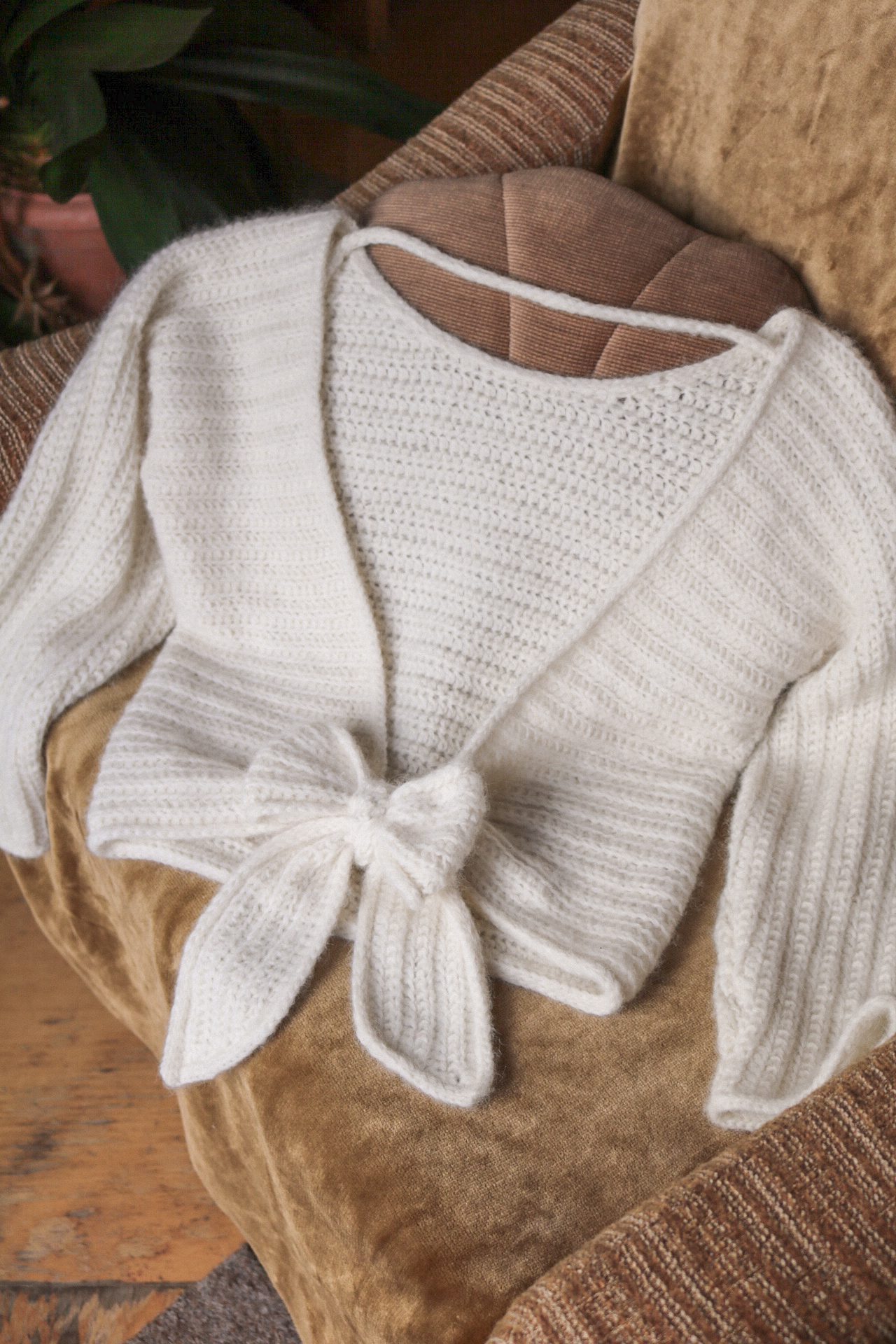 Cream crochet wrap sweater laid flat on a velvet chair, showing the ribbed texture of alternating front and back loop half double crochet