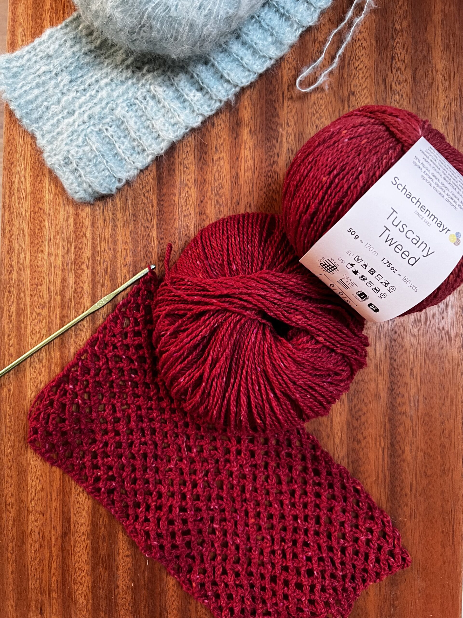 Dark red tweed swatch worked in open mesh stitch beside a pale blue mohair swatch in a solid fabric, with the tweed ball band showing