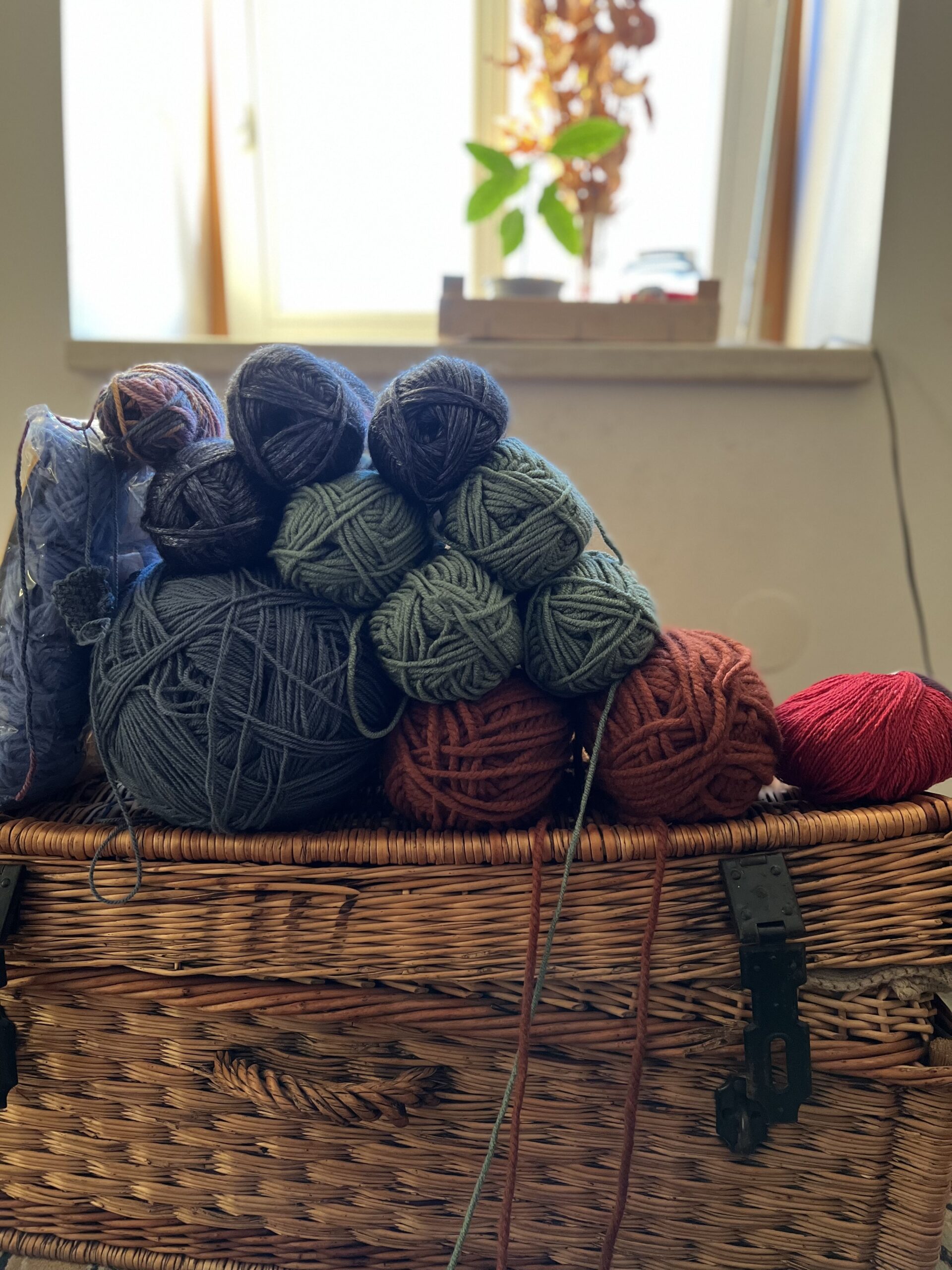 Several balls of wound yarn in cream and natural tones resting on a tartan box, ready to crochet from