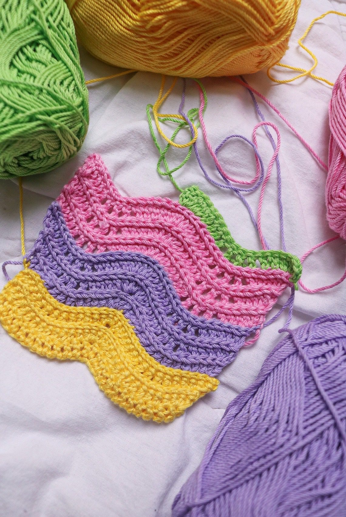 A crocheted gauge swatch worked in a wavy textured stitch in multicoloured yarn, big enough to measure across the middle