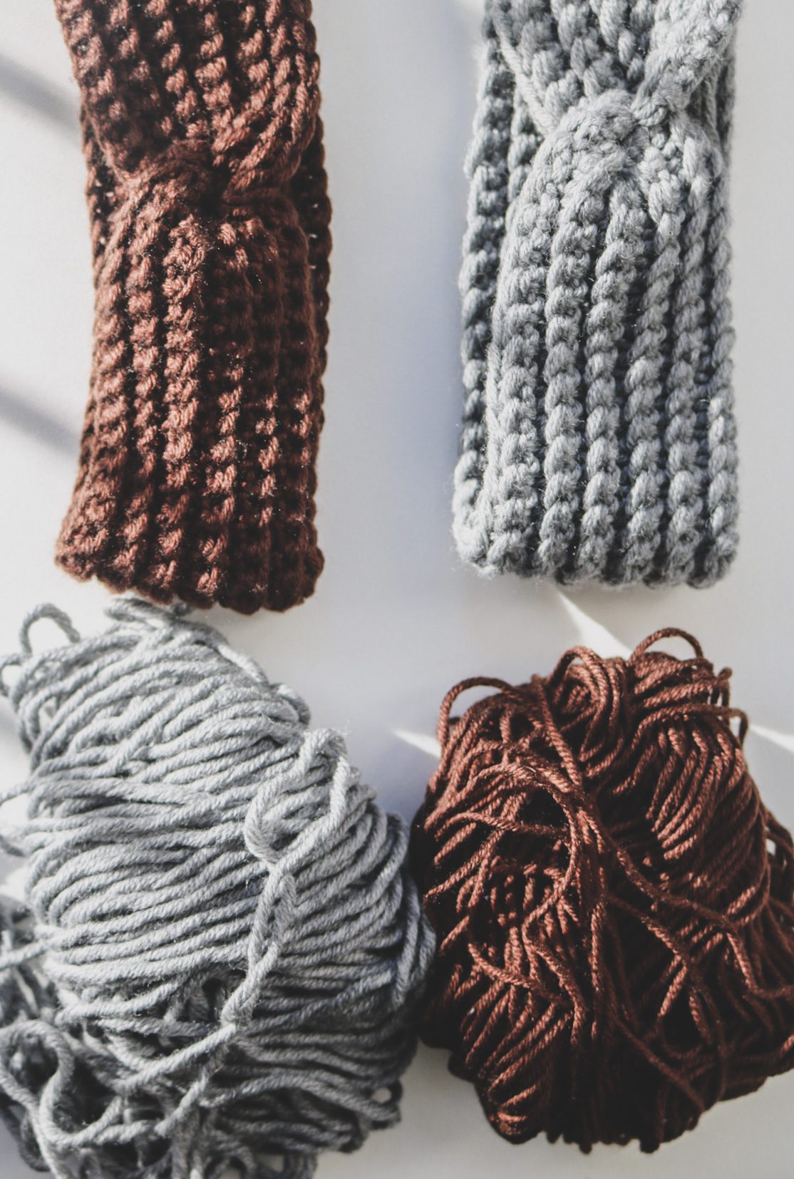 Two thin crocheted headbands, one grey and one brown, lying next to the balls of yarn each was made from, showing how the same pattern reads differently in two yarns
