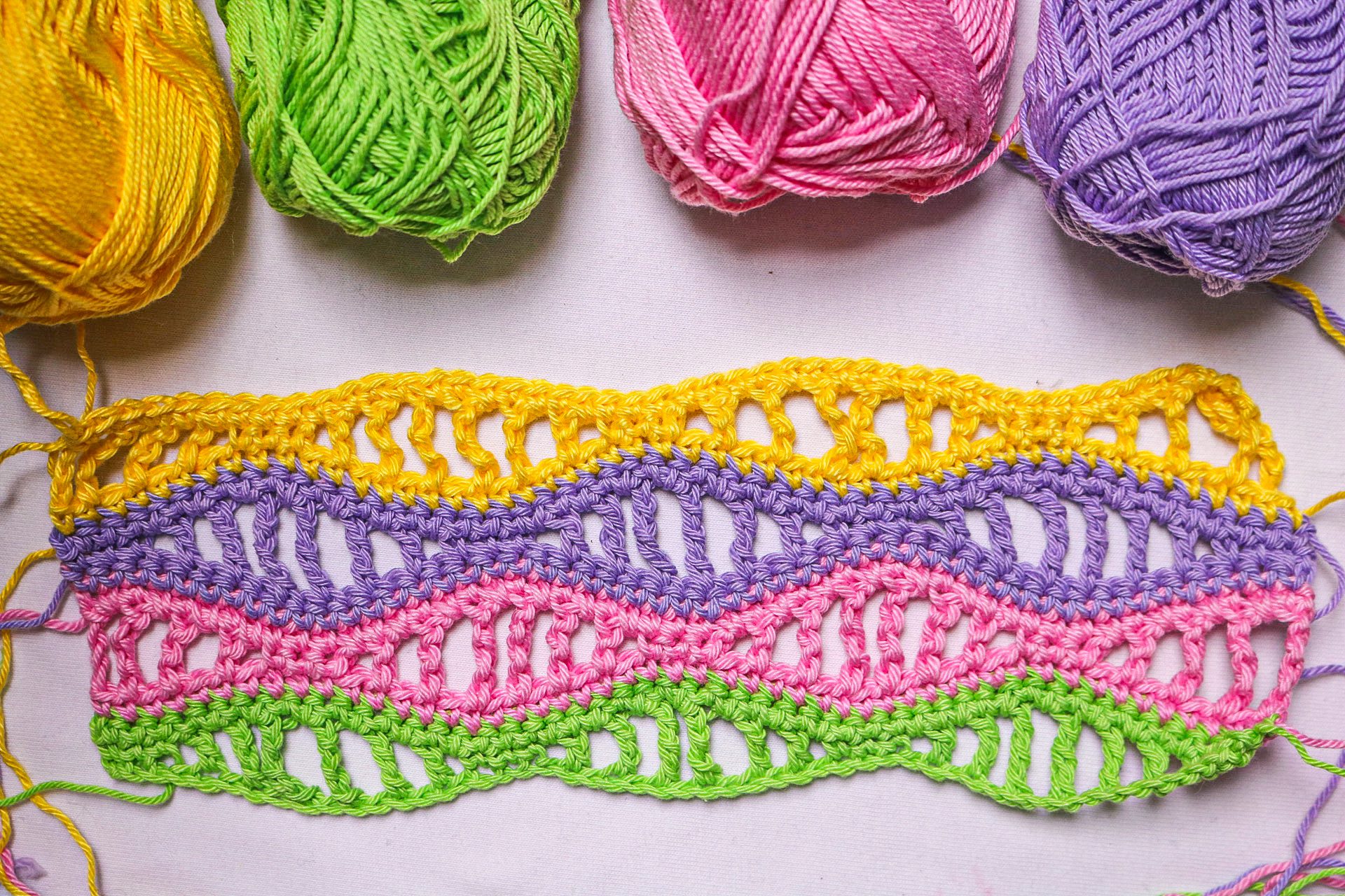 A multicoloured crochet swatch in a textured stitch beside the variegated yarns it was made from, showing how colour repeats stack up across a row