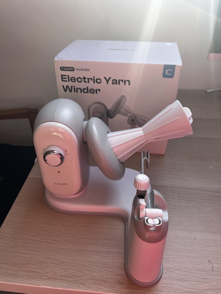The Caydo A1 Pro Max electric yarn winder set up on a table in front of its box, showing the tension dial, the spindle and the yarn guide arm