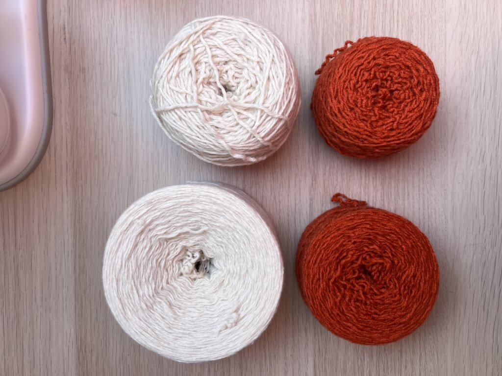 Four wound yarn cakes in cream and rust laid out on a table, showing the flat sides and centre pull holes the winder produces