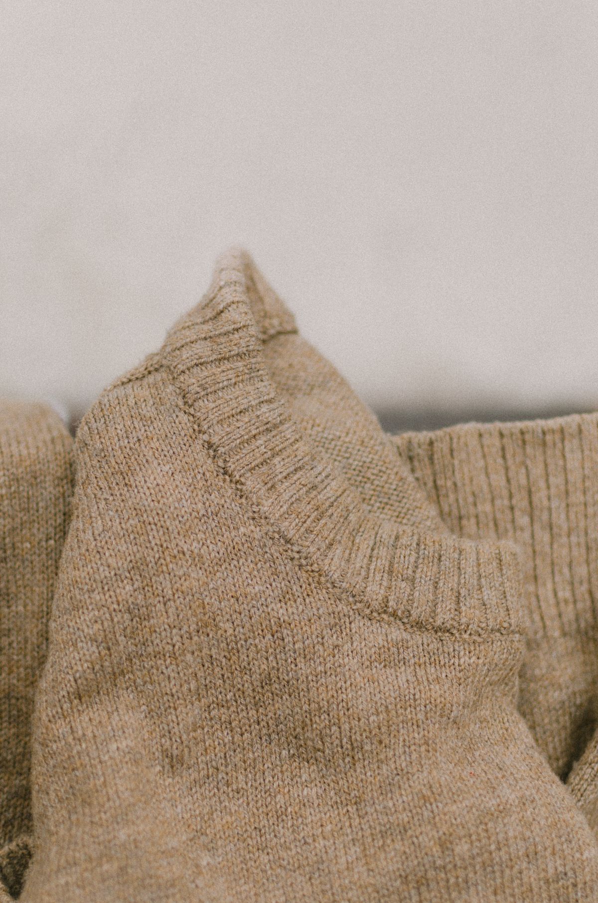 Close-up of a beige knit sweater neckline showing the ribbed collar and smooth stocking stitch of a knit-to-shape, fully fashioned garment